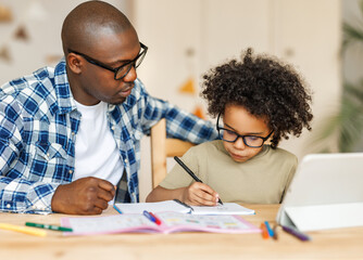 Naklejka premium Ethnic dad helps son to do homework at home.