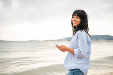 Smiling woman holding smart phone by sea at beach