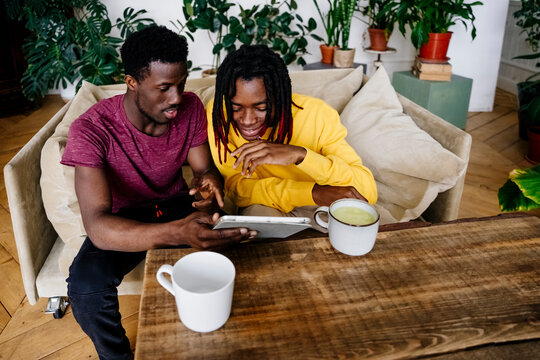 Smiling man sharing tablet PC with friend sitting at home