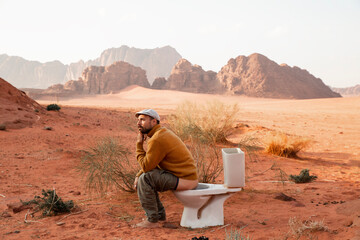 Contemplative man sitting on toilet seat and defecating in desert