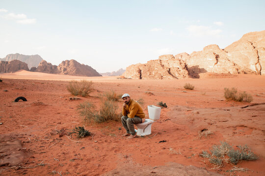 Thoughtful man sitting on toilet seat and defecating in desert