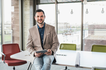 Confident businessman with tablet PC sitting on table in office