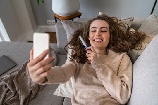 Happy young woman showing pregnancy testing kit on video call at home