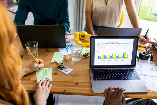 Businesswoman writing in paper by graph data on desk at office