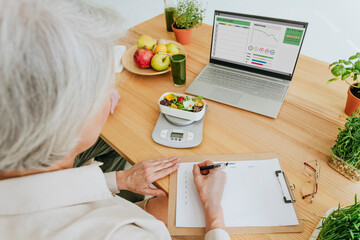 Nutritionist writing on clipboard with diet food on table at home