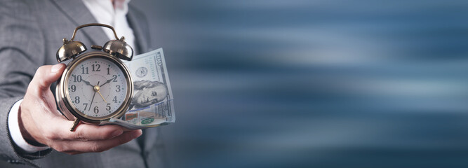 Businessman holding alarm clock and dollar banknotes.