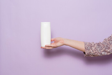 Woman's hand holding packaging of shampoo or conditioner, location. Cosmetic product in bottle