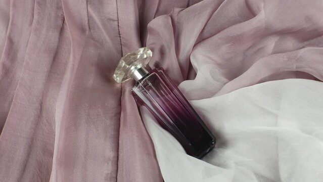 A bottle of women's perfume on a dusty rose-coloured fabric background. A bottle of luxury perfume on a pink abstract background in different shades. Flat lay. Close-up
