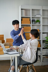 A cheerful Asian man, an online shop owner, is giving a high five to his girlfriend