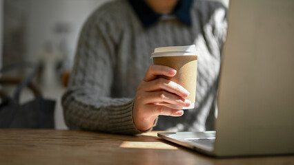 Close-up image of a female freelancer sipping coffee while responding to emails on her laptop