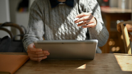 Close-up image of a female using her digital tablet while sitting in a cozy coffee shop.