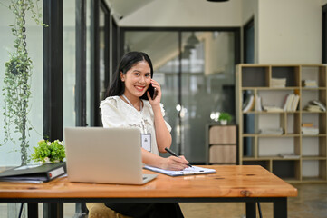 Attractive of young Asian businesswoman is talking on the phone at her desk