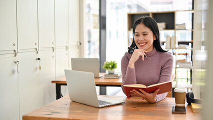 Obraz na płótnie Canvas Happy Asian female college student looking her laptop screen, doing homework