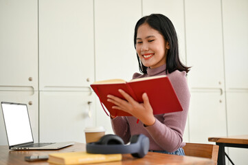 Naklejka premium A female college student researched information in a book while remote working at the coffee shop.