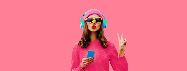 Trendy colorful portrait of stylish young woman in headphones listening to music with phone and...