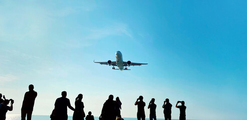 Fototapeta na wymiar Silhouette of group of unknown people tourists take pictures a landing passenger airplane flying in blue sky background