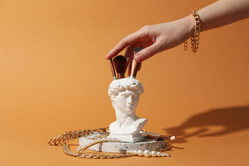 Jewelry and makeup concept with ancient head on brown background