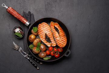 Grilled salmon steaks and potatoes sizzling in a frying pan