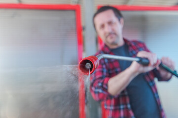 Man washing car with water gun in carwash self-service. Soap sud, wax and water drops covering...