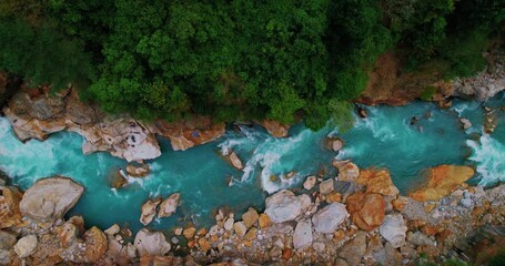 Aerial view of serene blue river winding through lush green forests and glistening stones. Experience the tranquility of nature captured from Manaslu Circuit, Nepal. 4K.