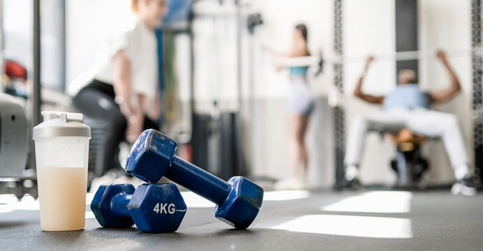 Dumbbells with bottle of protein drink placed on floor in sports club