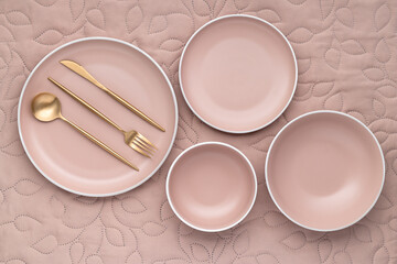 A set of cream color plates of different sizes on table, top view. Golden cutlery and serving...
