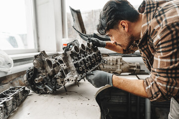 Workman disassembling car engine at the working table of the car service garage