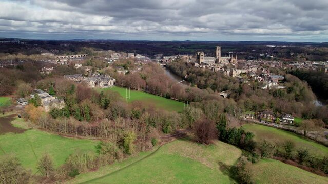 Drone flies over playing fields towards beautiful city of Durham UK