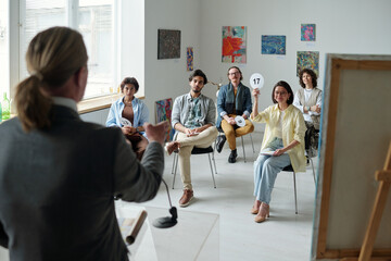 Group of people sitting at auction in art gallery and buying painting of modern art