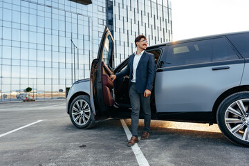 Young handsome businessman in a suit comes out of the luxury car