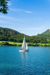 Sailing boat in the lake against the background of mountains and green forest. Sailboat floating on...