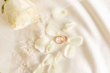 Two gold wedding rings and tea rose on a satin background with pearl beads. A copy space. Wedding...