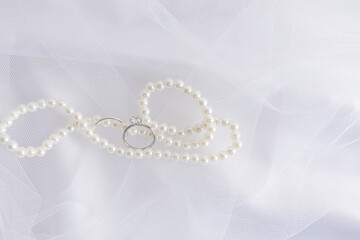 A chic background for wedding design. An elegant white pearl necklace and two white gold diamond engagement rings.
