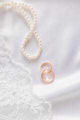 Vertical view of two gold wedding rings, part of the lace of the bride's veil and pearl beads. Layout of the design of invitations, postcards, albums.