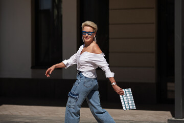 Woman runs on street of city, in hurry is late, with short hair in white shirt and cargo jeans...