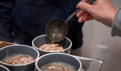 Home cooking Vietnamese soup dish Pho. Hand holding spoon pouring soup into the bowl with meat and noodles.