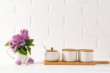 Beautiful kitchen background in light colors in a minimalist style. Three ceramic jars for storage on a wooden board and a bouquet of lilacs in a jug.