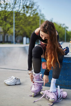 Young roller blader putting on aggressive inline skates. Female skater preparing for a ride in a skatepark in summer