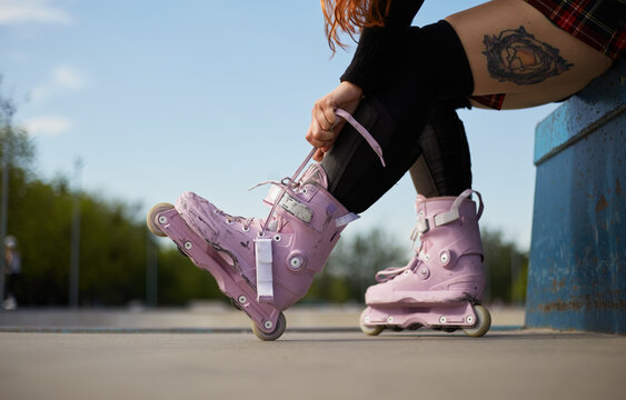 Aggressive inline skater girl tying laces on modern roller blades in a skatepark. Young female athlete preparing for a ride on skates