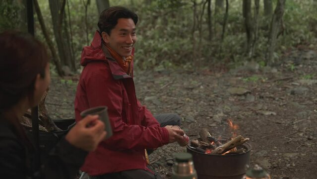 캠핑장에서 모닥불을 피우며 맞은편 친구와 대화하는 부부 