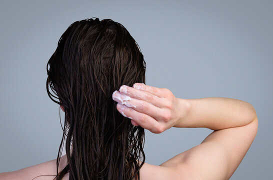 Hair care and treatment. Young girl applying a therapeutic mask to wet hair on a gray background.