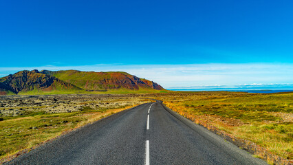 Panoramic over a paved road and Icelandic colorful and wild landscape with fjords and sea at summer time, West Iceland