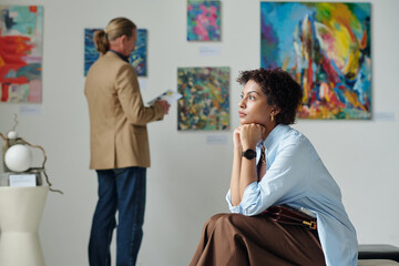 Young pensive woman sitting on couch and resting after exhibition in art gallery