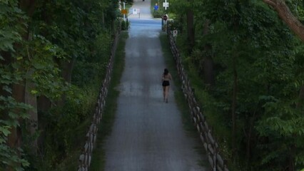 Woman running on a shaded forest path. Cardiovascular exercise theme. Aerial shot between trees.