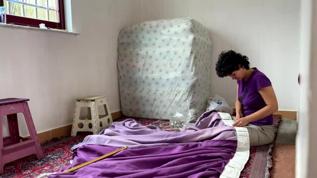 Beautiful Persian girl woman sewing violet curtain purple color at home in a room with window in village rural life hand made needle work traditional skill design craft fabric tailoring attach textile