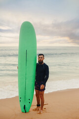 Fototapeta na wymiar Young bearded man with surfboard standing near a beach. Man with surfing board outdoors on a summer day.