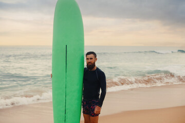 Fototapeta na wymiar Surfer holding surf board on the beach at sunset. Happy man guy having fun doing extreme sport