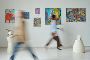 Blurred motion of people passing through the paintings on the wall in art gallery