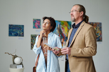 Art lovers enjoying modern art in gallery, they standing and examining paintings on the wall