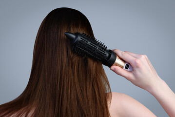 Young girl drying her hair with a hair dryer-comb on a gray background.
